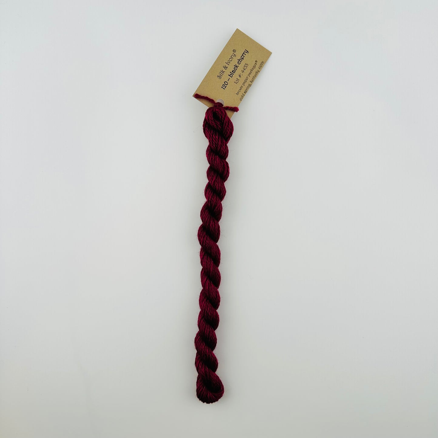 30 yard skein of silk & Ivory in the color 120 Black Cherry with brown tag laying flat on white background