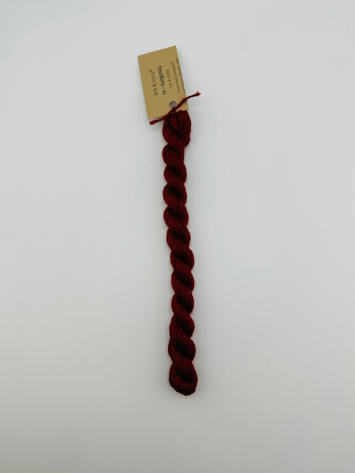 30 yard skein of silk & Ivory in the color 14 Burgundy with brown tag laying flat on white background
