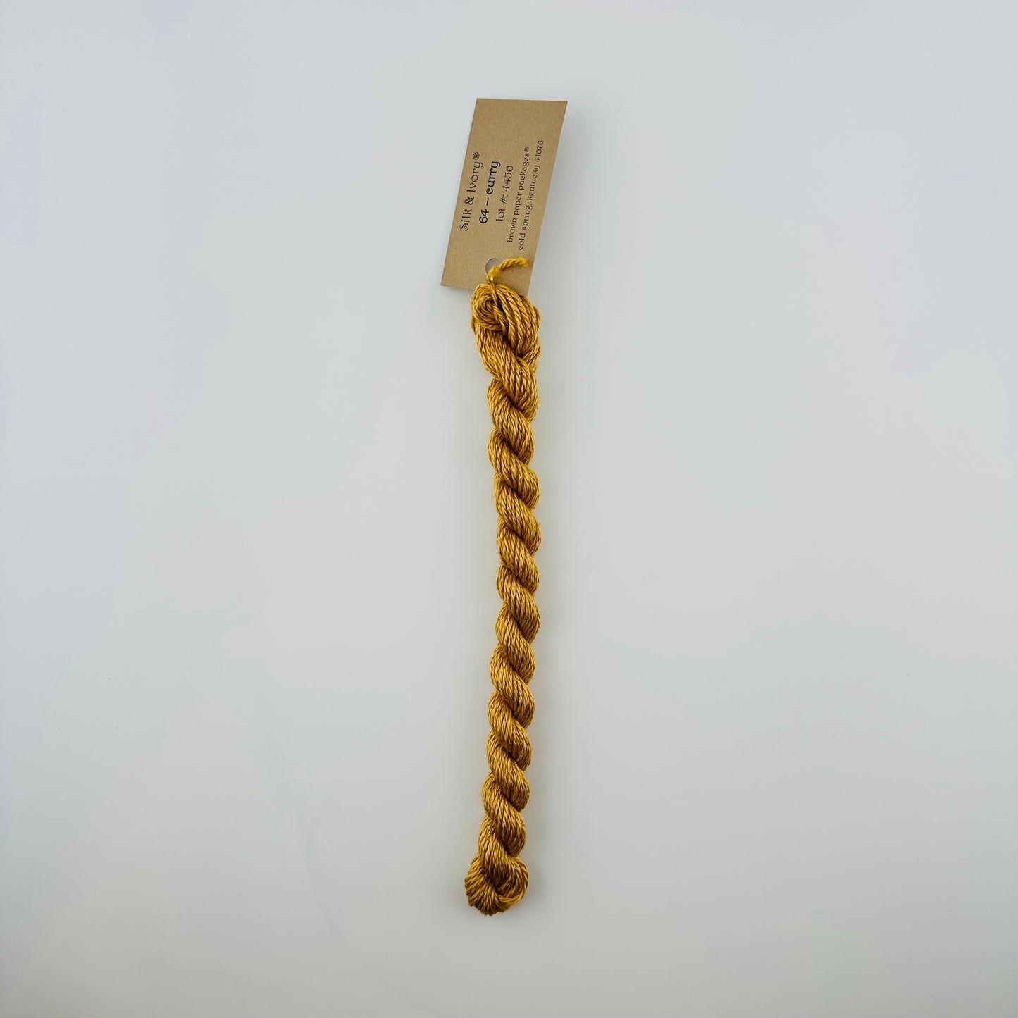 30 yard skein of silk & Ivory in the color 64 Curry with brown tag laying flat on white background
