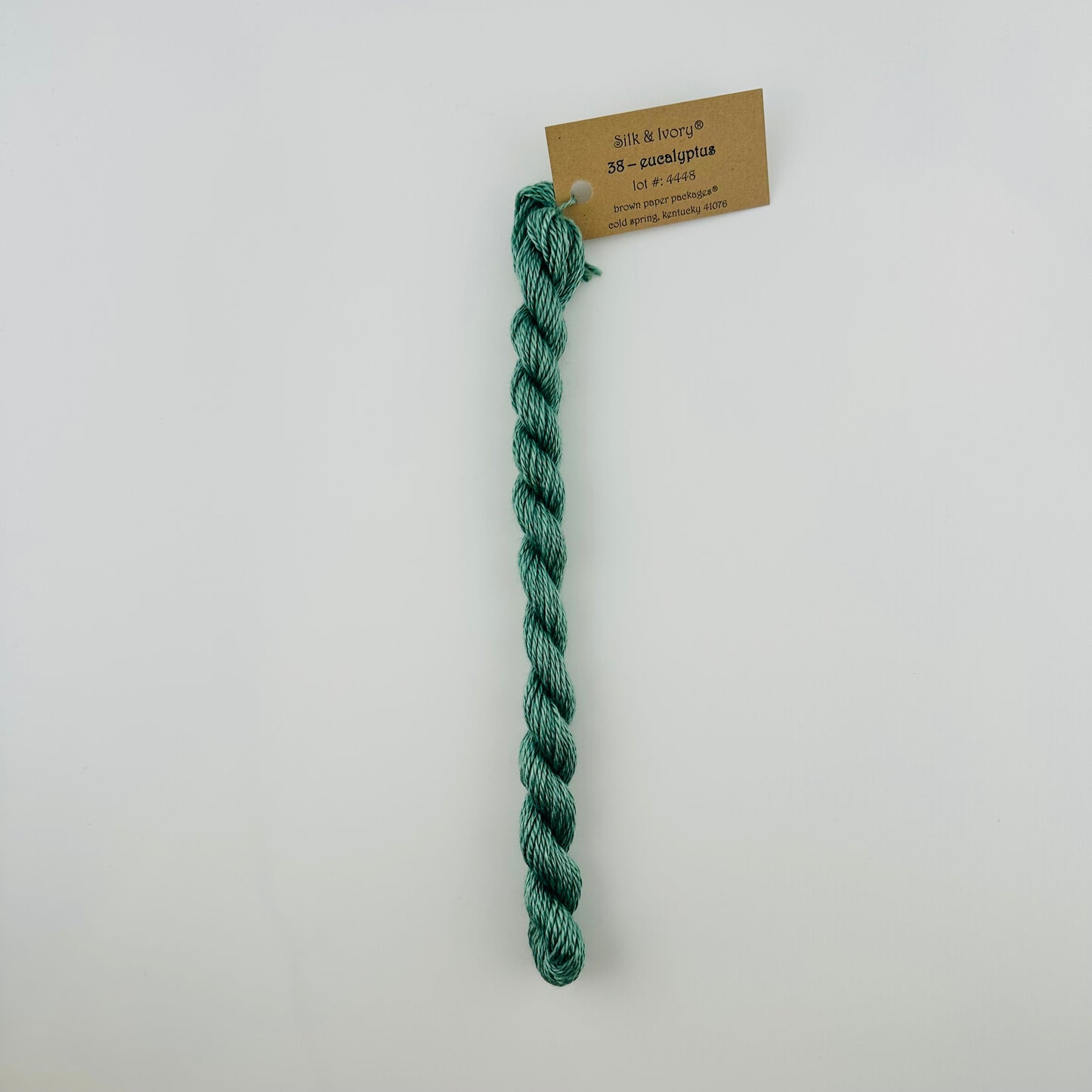30 yard skein of silk & Ivory in the color 38 Eucalyptus with brown tag laying flat on white background