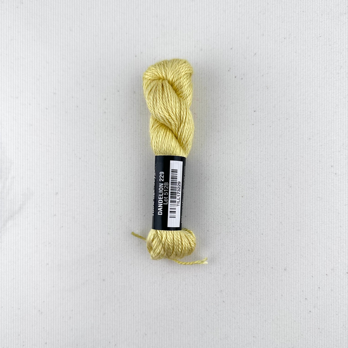 30 yard skein of Pepper Pot Silk needlepoint thread in a yellow variegated dandelion v229, with black and white label lying flat on white background