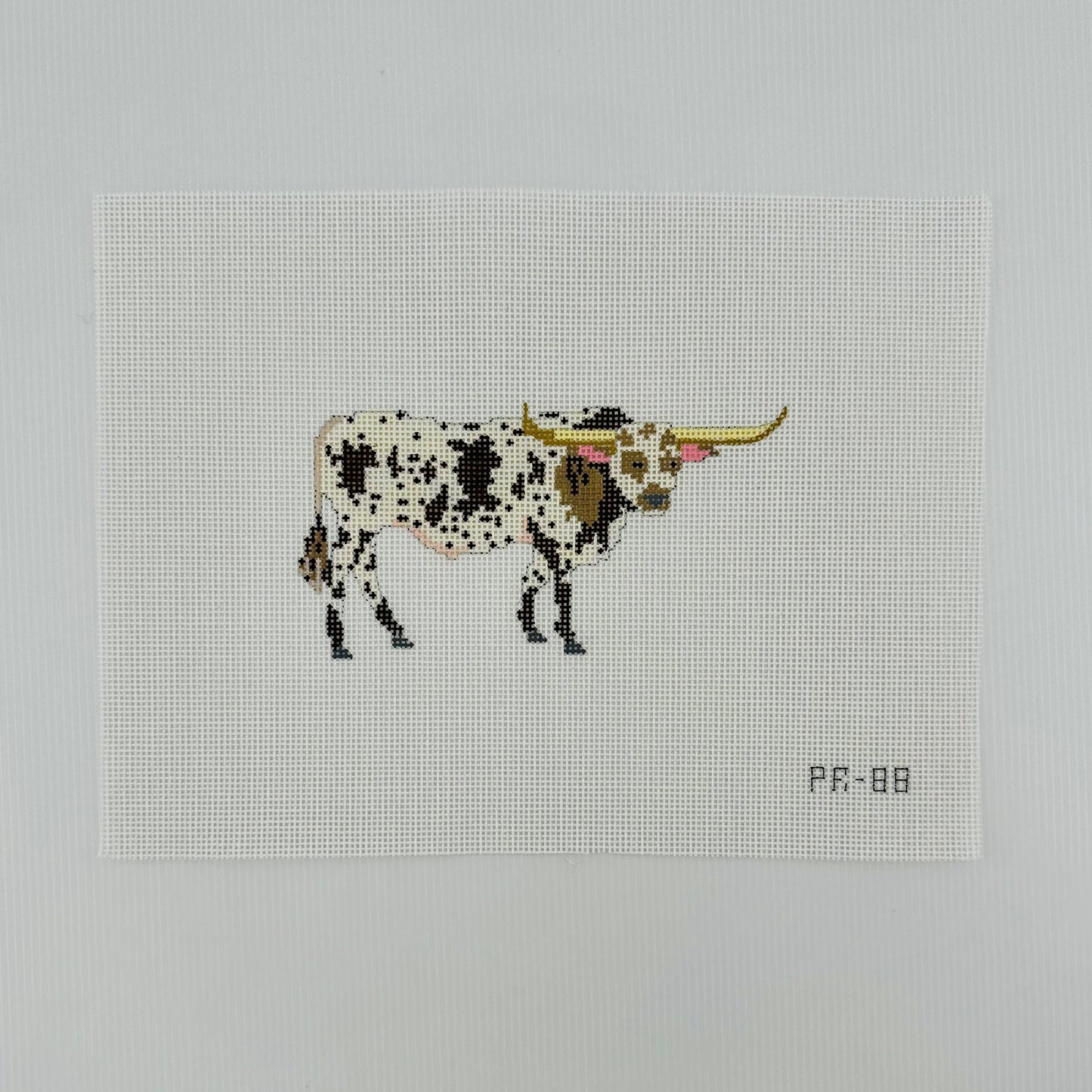 A needlepoint canvas featuring a brown and white spotted longhorn bull, displayed flat on a white background.