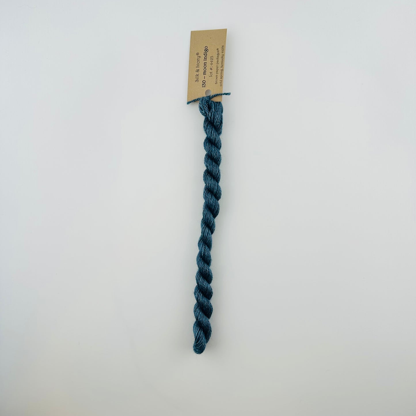 30 yard skein of silk & Ivory in the color 130 Moon Indigo with brown tag laying flat on white background