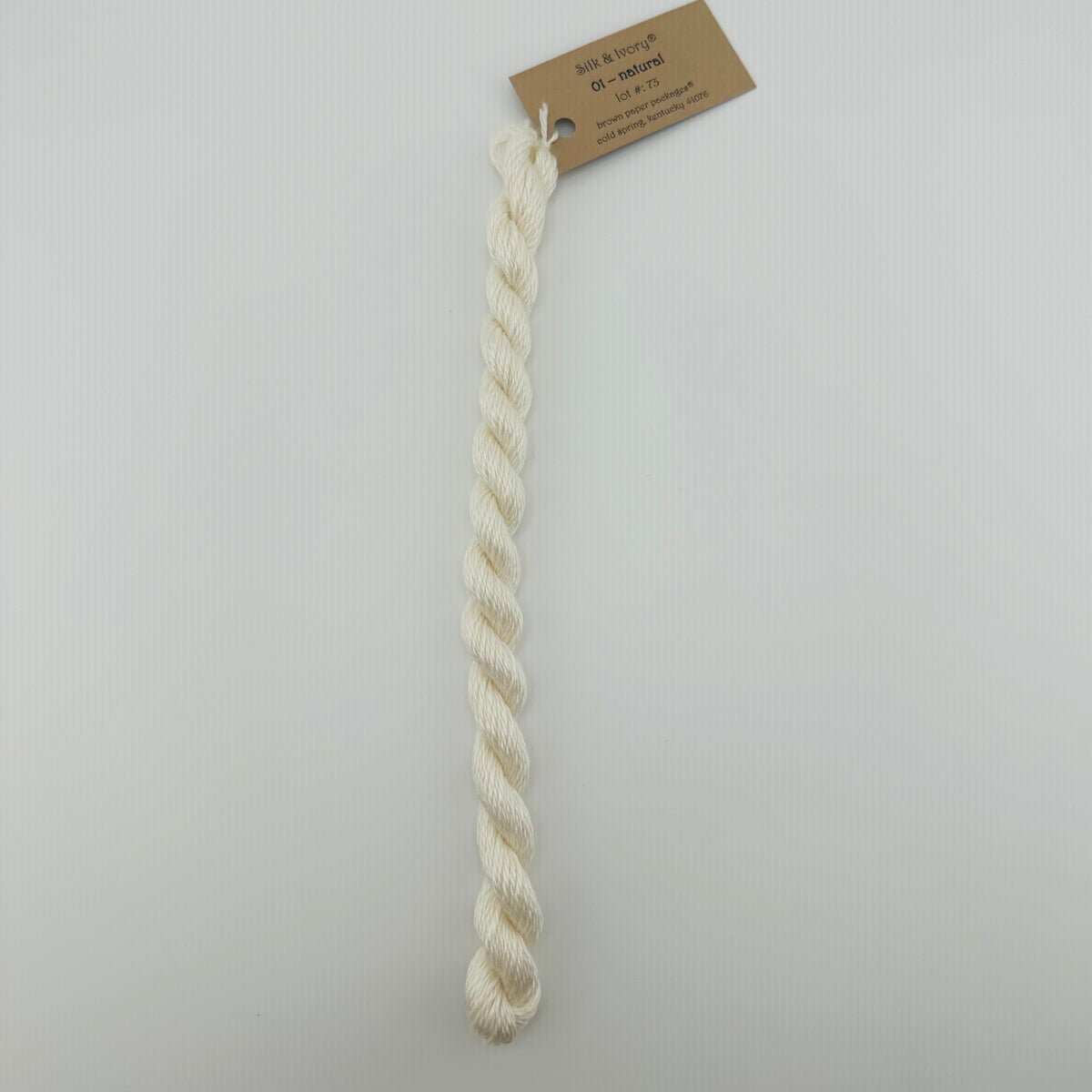 30 yard skein of silk & Ivory in the color 01 Natural with brown tag laying flat on white background