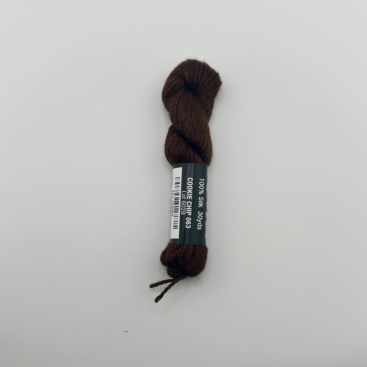 30 yard skein of Pepper Pot Silk needlepoint thread in cookie chip 063 brown with black and white label lying flat on white background