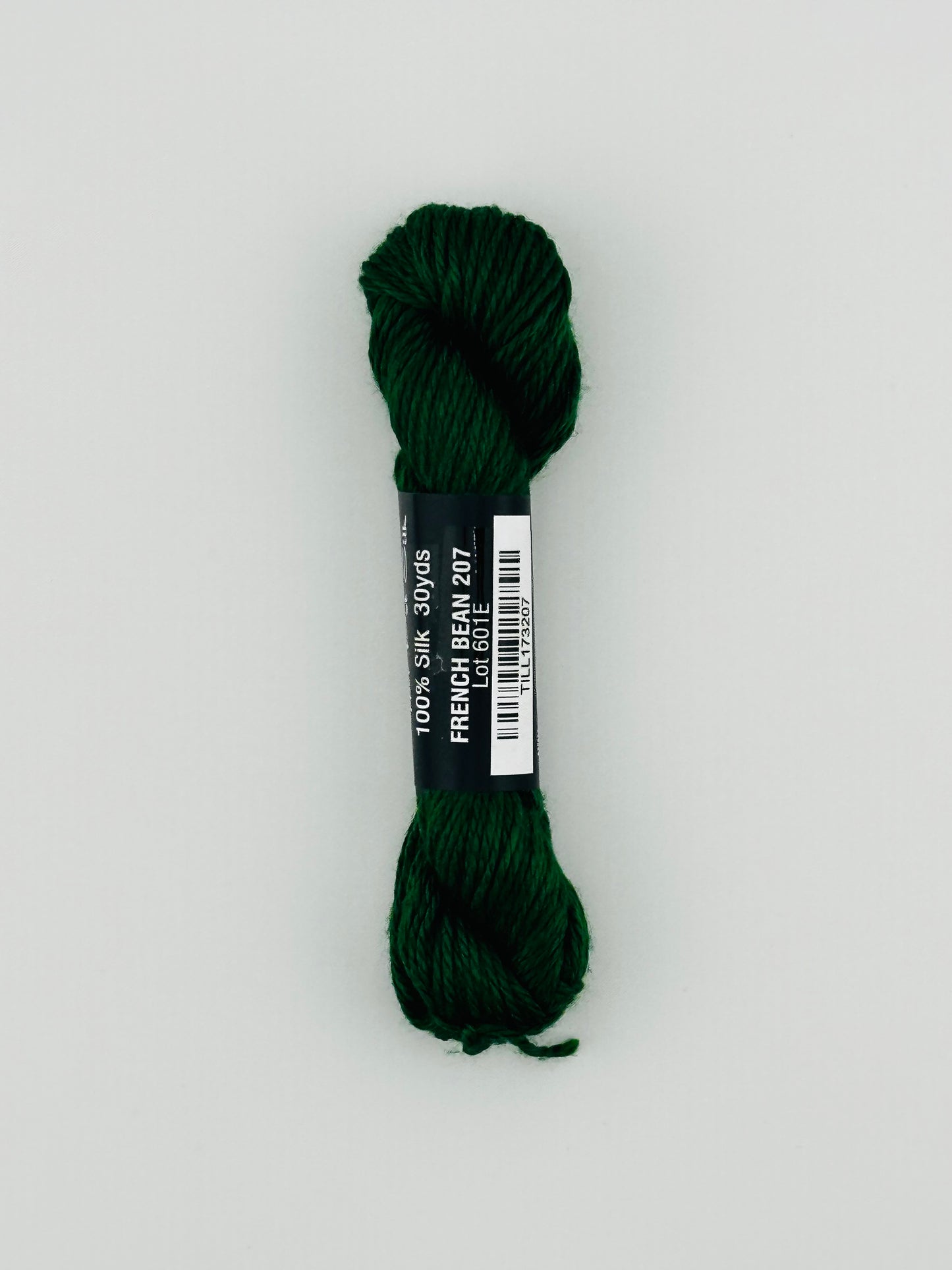 30 yard skein of Pepper Pot Silk needlepoint thread in french bean 207 green, with black and white label lying flat on white background