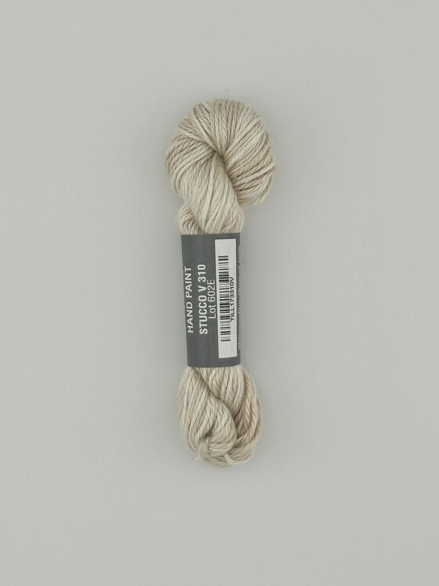 30 yard skein of Pepper Pot Silk variegated needlepoint thread in stucco v310 with black and white label lying flat on white background