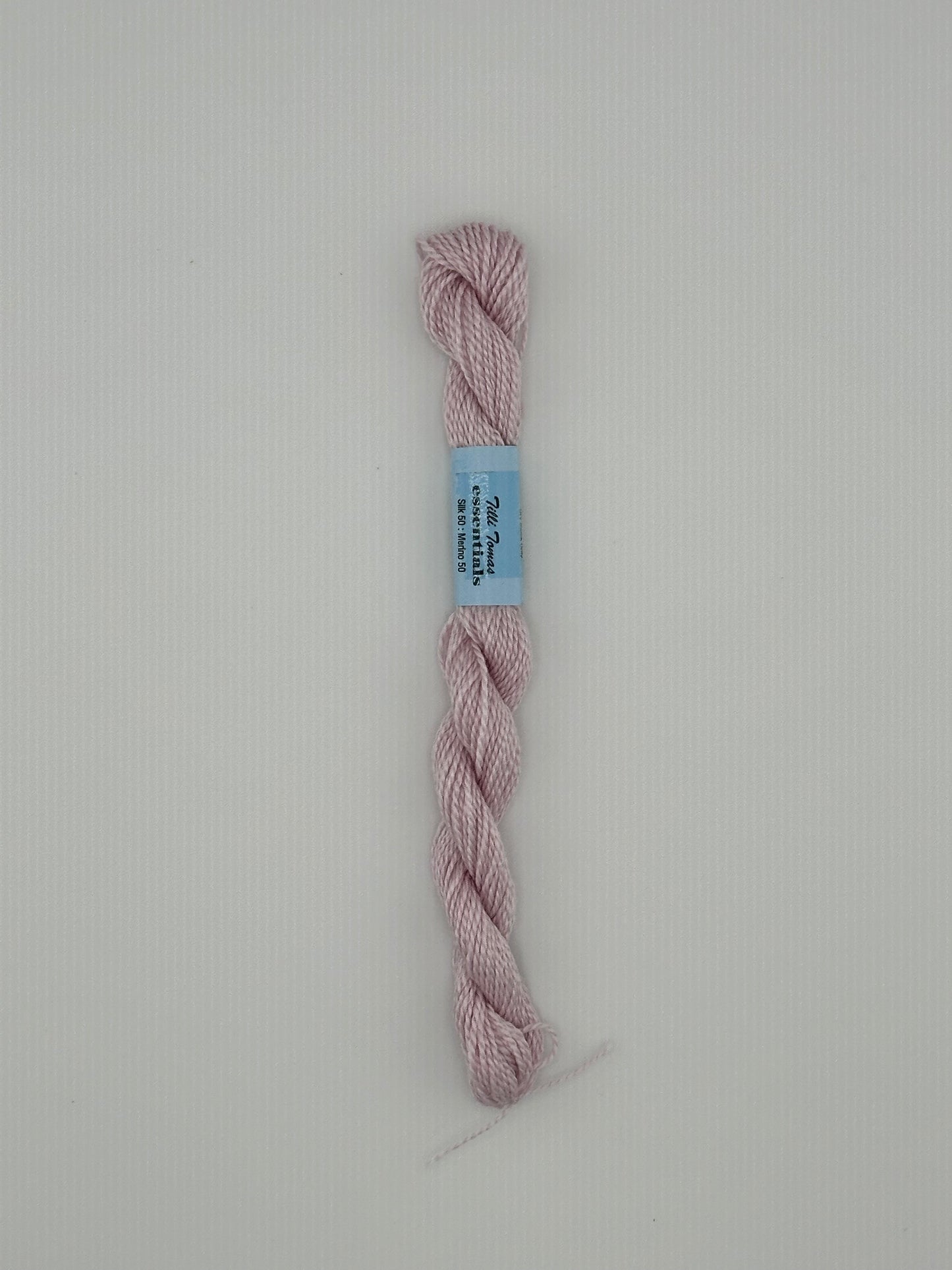 30 yard skein of essentials needlepoint thread in Petal S842 light pink, with blue label lying flat on white background.