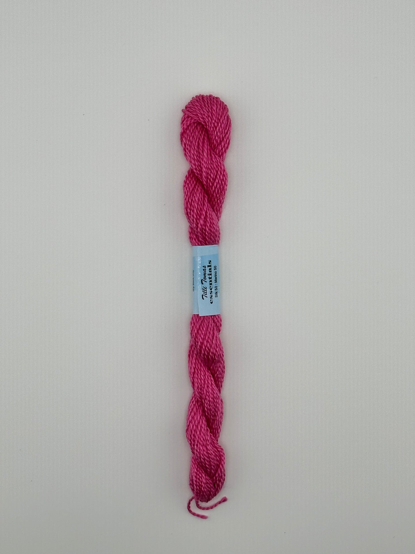 30 yard skein of essentials needlepoint thread in Ribbon S844 pink, with blue label lying flat on white background.