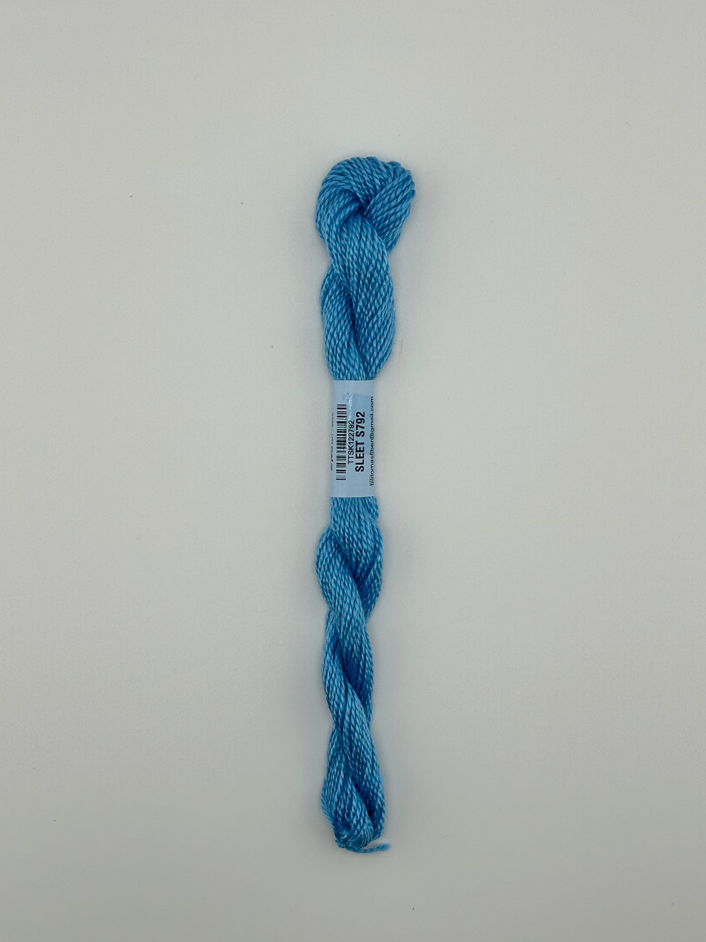 30 yard skein of essentials needlepoint thread in Sleet S792 blue, with blue label lying flat on white background