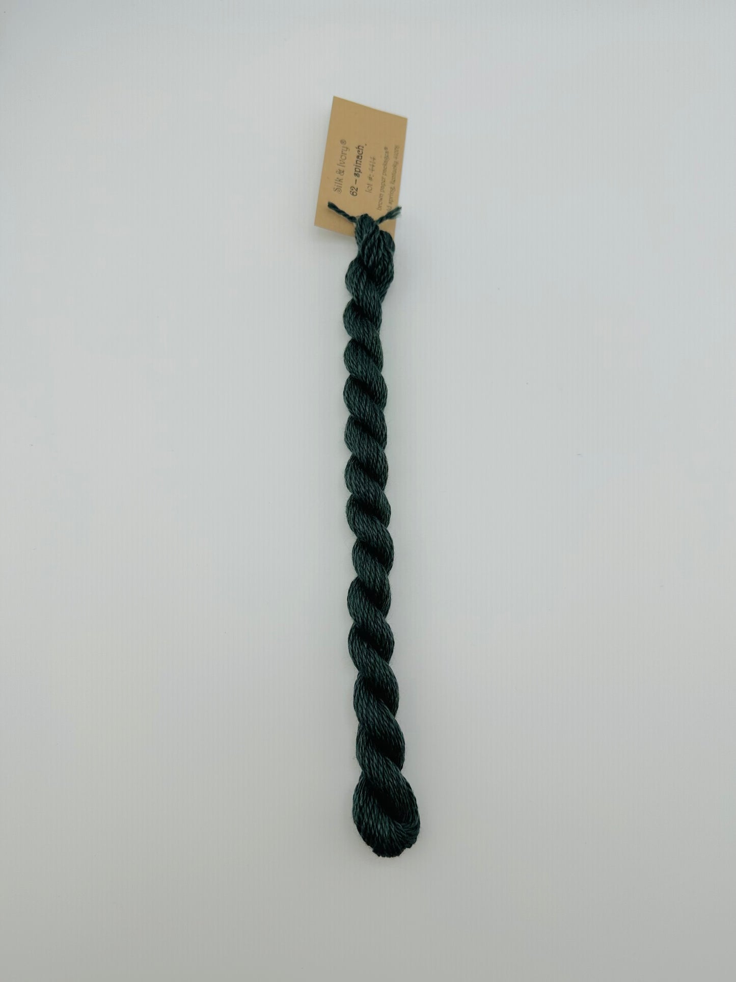 30 yard skein of silk & Ivory in the color 62 Spinach with brown tag laying flat on white background