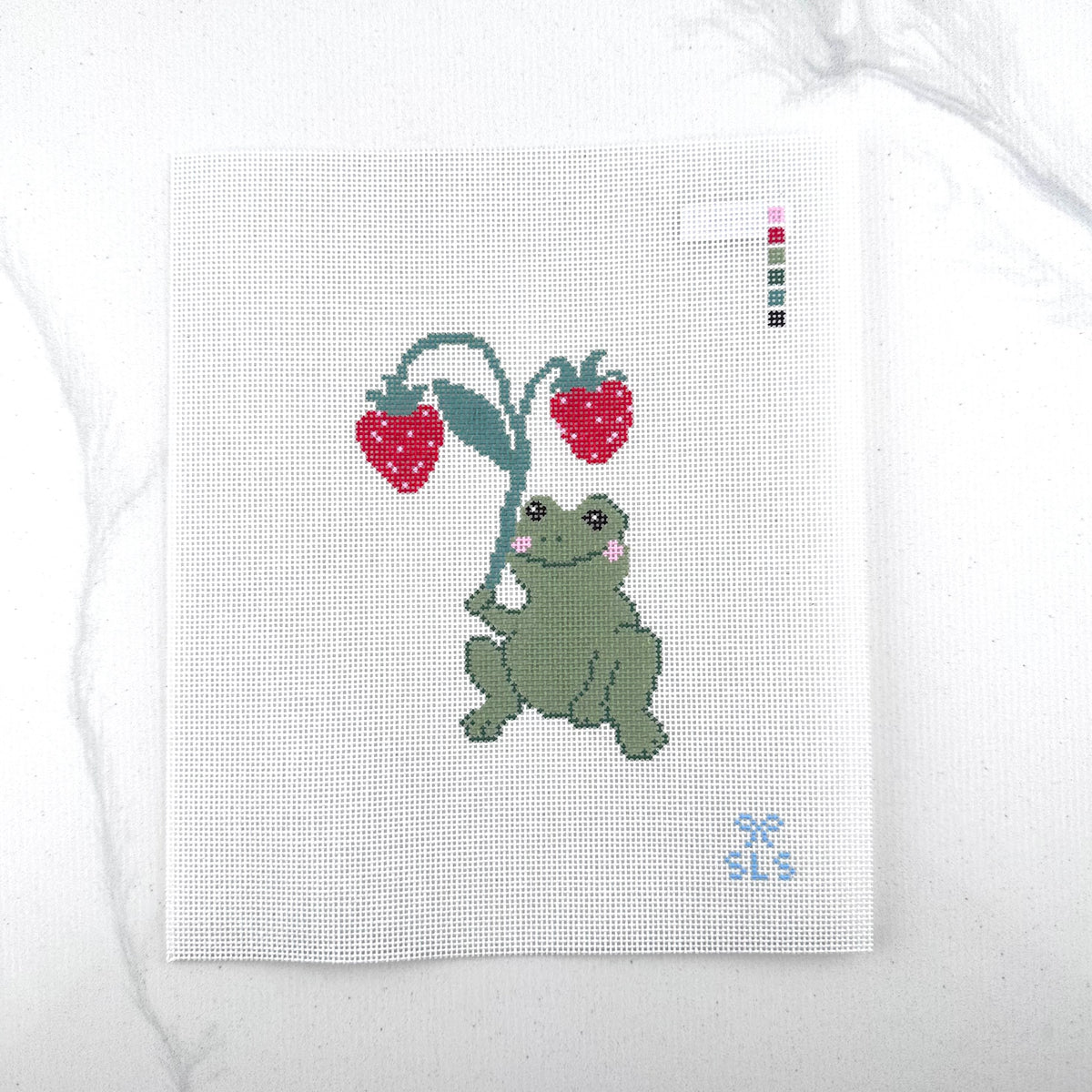 an 18 mesh needlepoint canvas featuring a design of a green frog holding a leafy plant with two red strawberries, photographed on a white background.