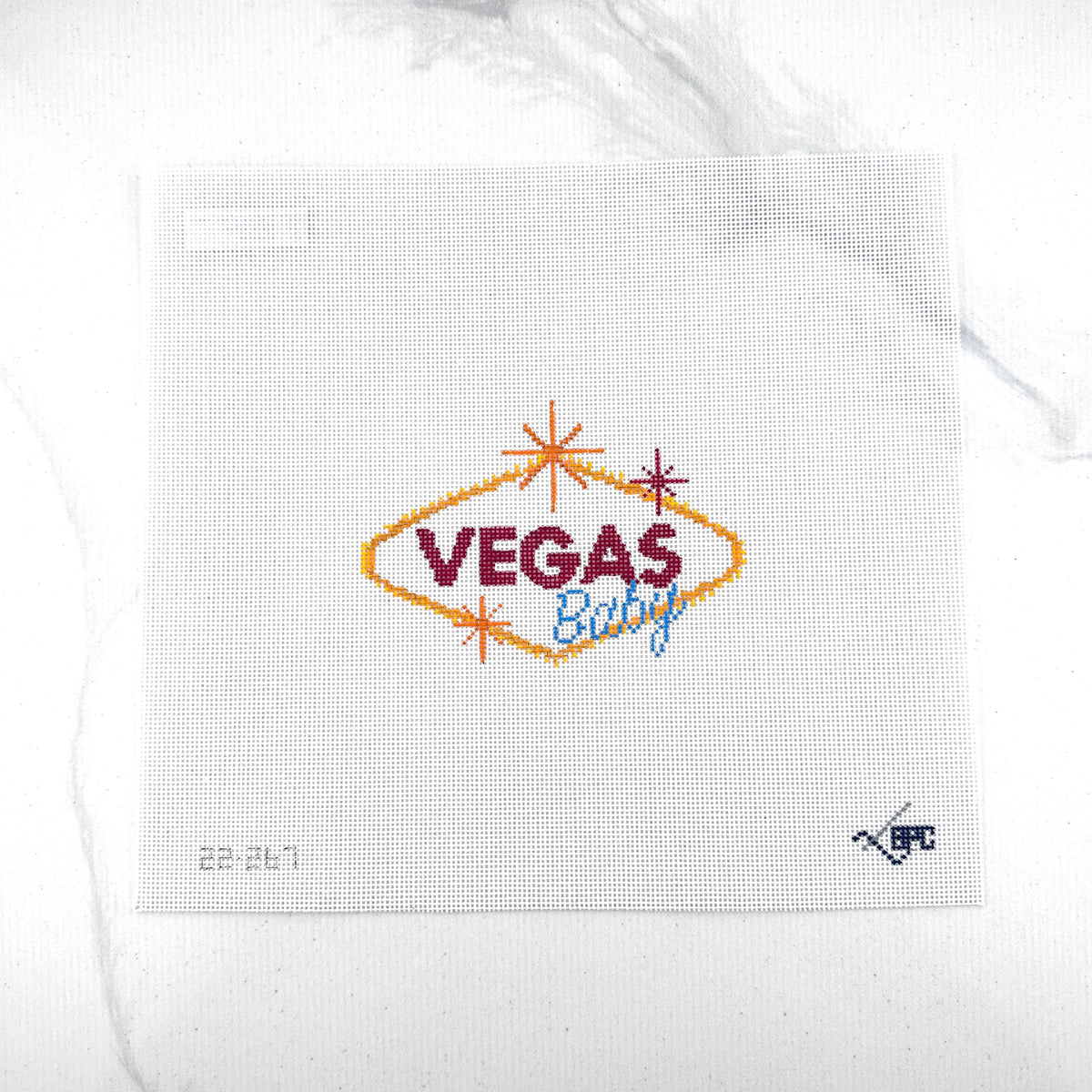 18 mesh needlepoint canvas featuring a 'Vegas Baby' design. The design includes a gold diamond outline, dark red 'VEGAS' text, and blue 'Baby' script, accented with small orange and red starbursts.