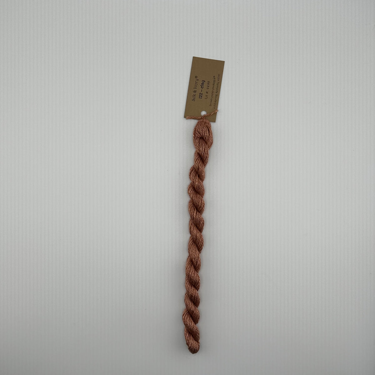 30 yard skein of silk & Ivory in the color 122 Clay with brown tag laying flat on white background