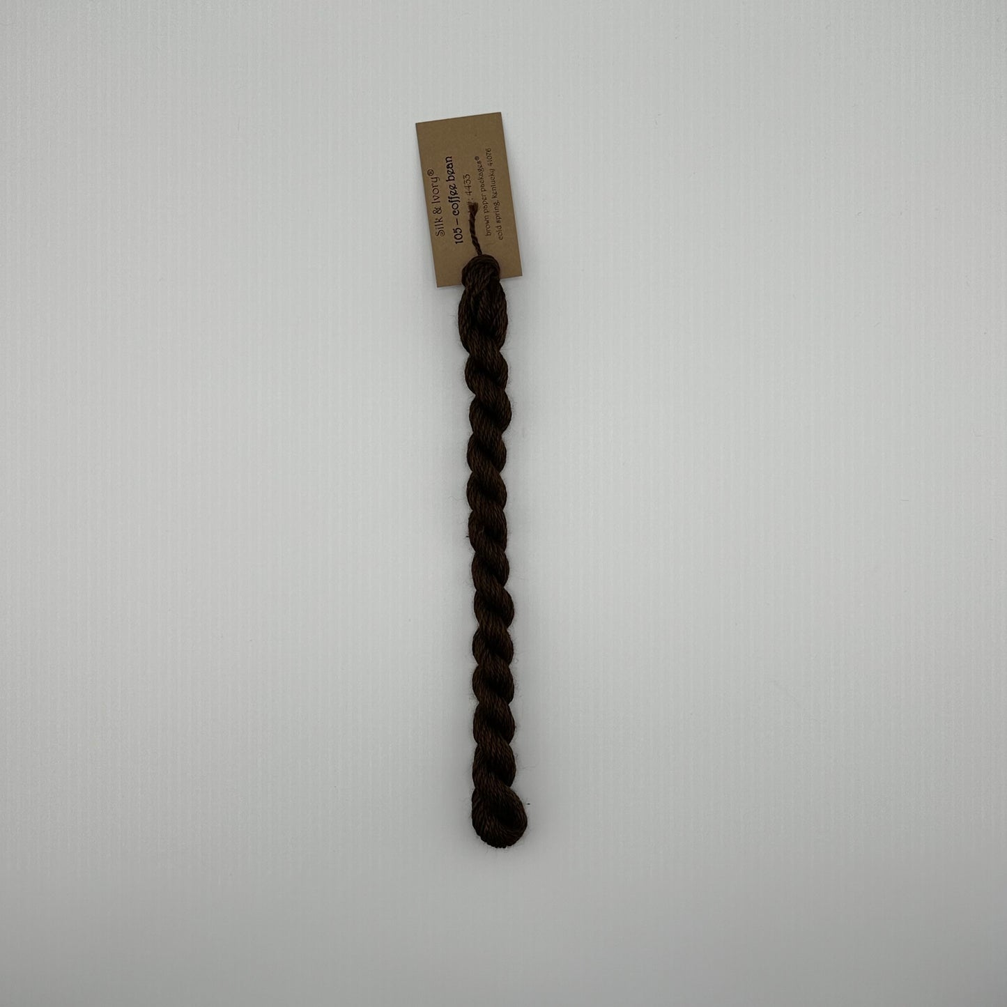 30 yard skein of silk & Ivory in the color 105 Coffee Bean with brown tag laying flat on white background