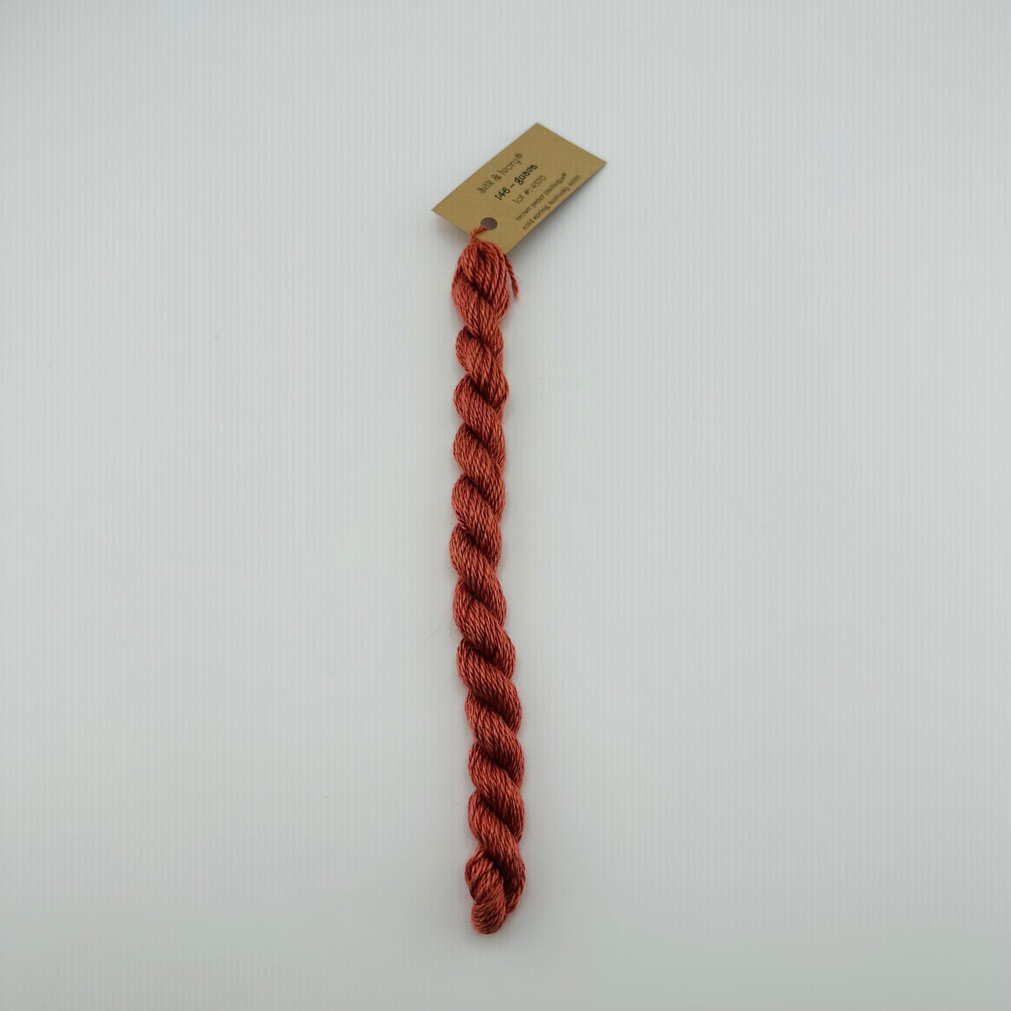 30 yard skein of silk & Ivory in the color 146 Guava with brown tag laying flat on white background