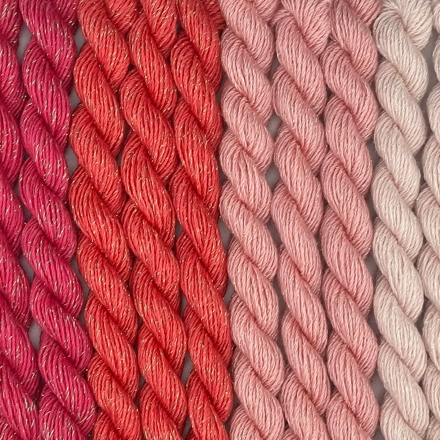 close-up of 10 skeins of Stardust Silk and Ivory needlepoint thread in four shades of pink including carnation 647, pink lemonade 611, pink cow 573, watermelon 550, lying side by side.