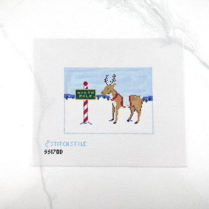 18 mesh needlepoint canvas featuring a Christmas scene with a brown reindeer wearing a red harness, standing next to a red-and-white striped pole with a green sign that reads 'NORTH POLE'. With the brand name 'STITCHSTYLE' and number 'S51700' printed in blue at the bottom left.