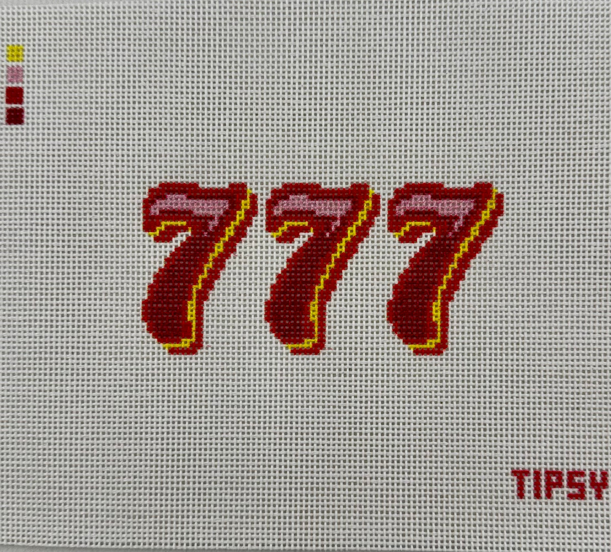A close-up of a needlepoint canvas showing the number 777 stitched in dark red and pink with a yellow outline, on a white 18 mesh grid. The brand name 'TIPSY' is visible in the bottom right corner.