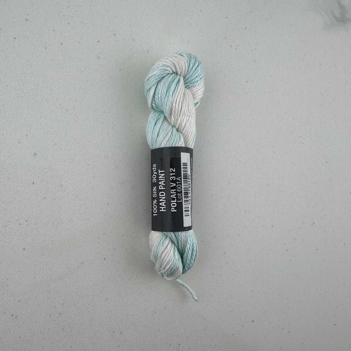 30 yard skein of Pepper Pot Silk needlepoint thread in a blue and white variegated polar v312, with black and white label lying flat on white background