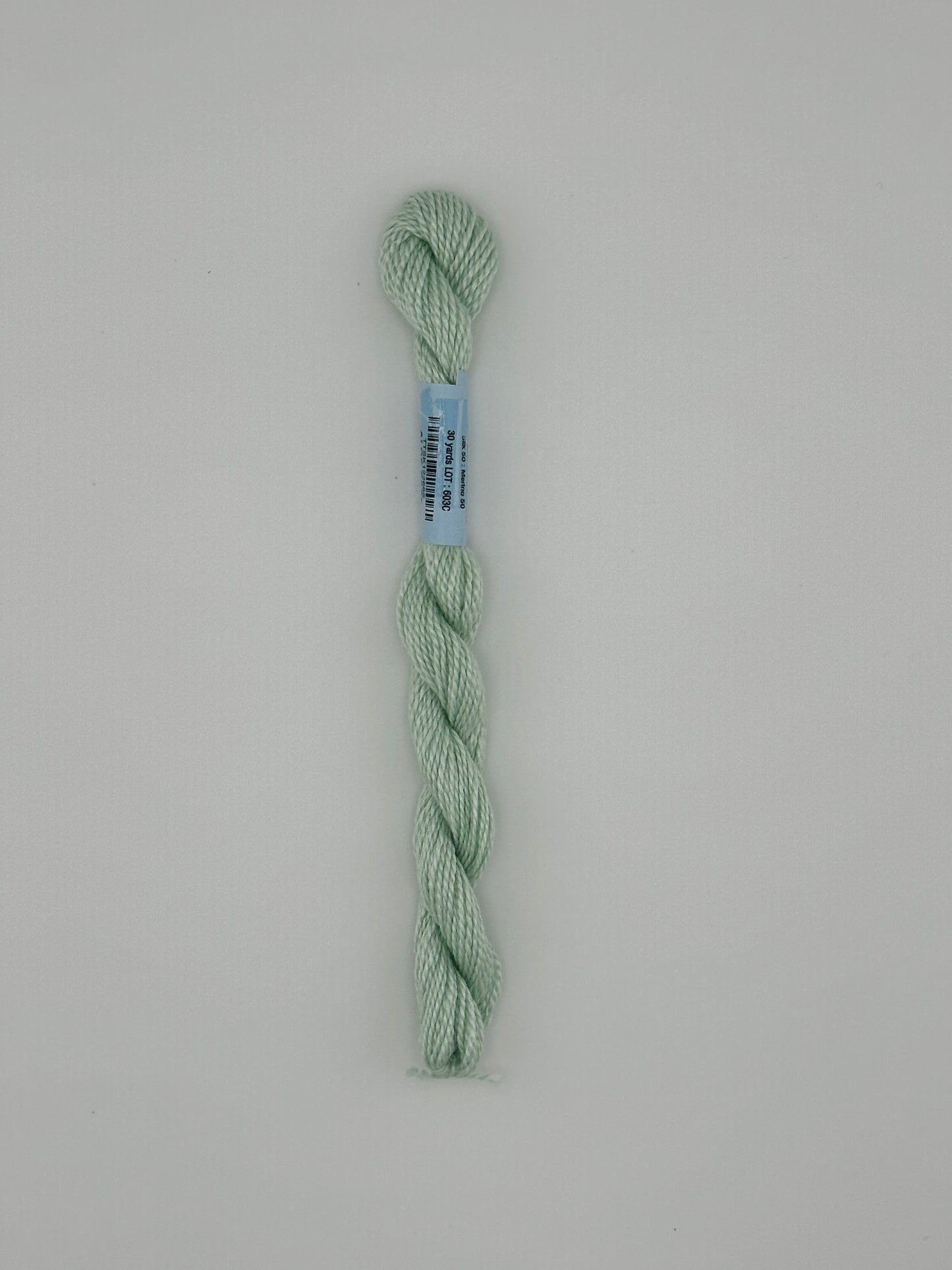 30 yard skein of essentials needlepoint thread in Aloe S685 green, with blue label lying flat on white background