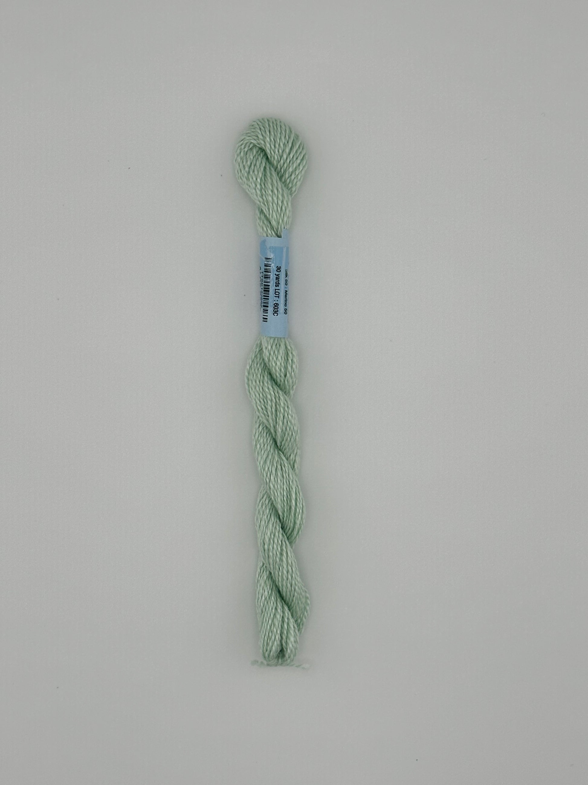30 yard skein of essentials needlepoint thread in Aloe S685 green, with blue label lying flat on white background