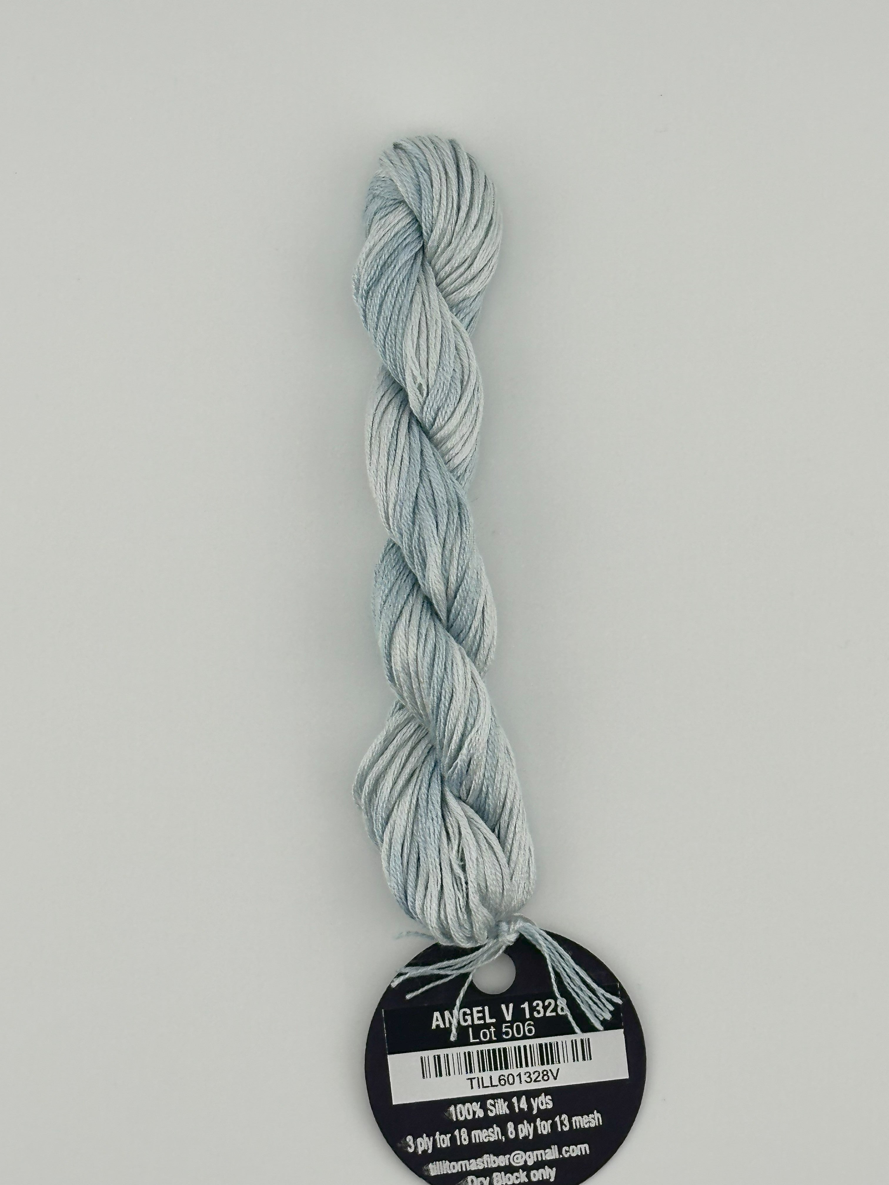 14 yard skein Planet Earth Silk 4 Ply needlepoint thread, in angel v 1328, with round black and white label lying flat on white background.
