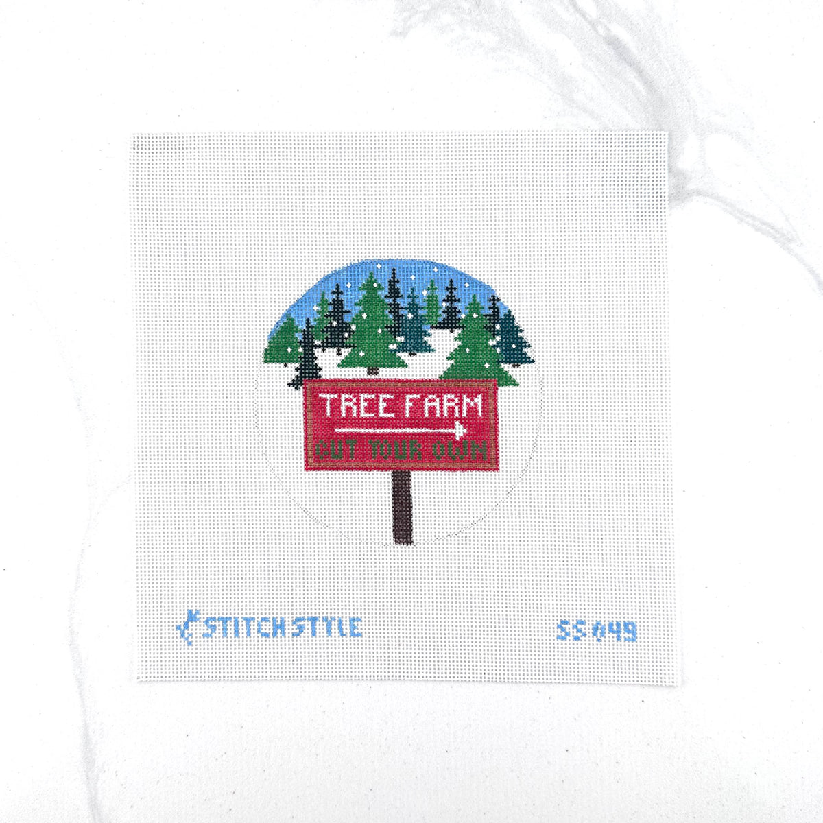 18 mesh needlepoint canvas featuring a design of a red 'Tree Farm' sign with a white arrow pointing right, set against a snowy pine tree landscape under a blue sky. The canvas is displayed on a white background with Stitch-Style branding and product code printed on the bottom.