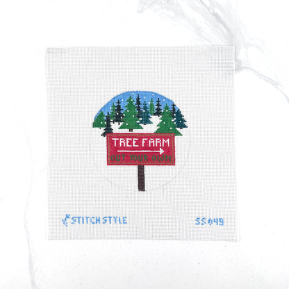 18 mesh needlepoint canvas featuring a design of a red 'Tree Farm' sign with a white arrow pointing right, set against a snowy pine tree landscape under a blue sky. The canvas is displayed on a white background with Stitch-Style branding and product code printed on the bottom.