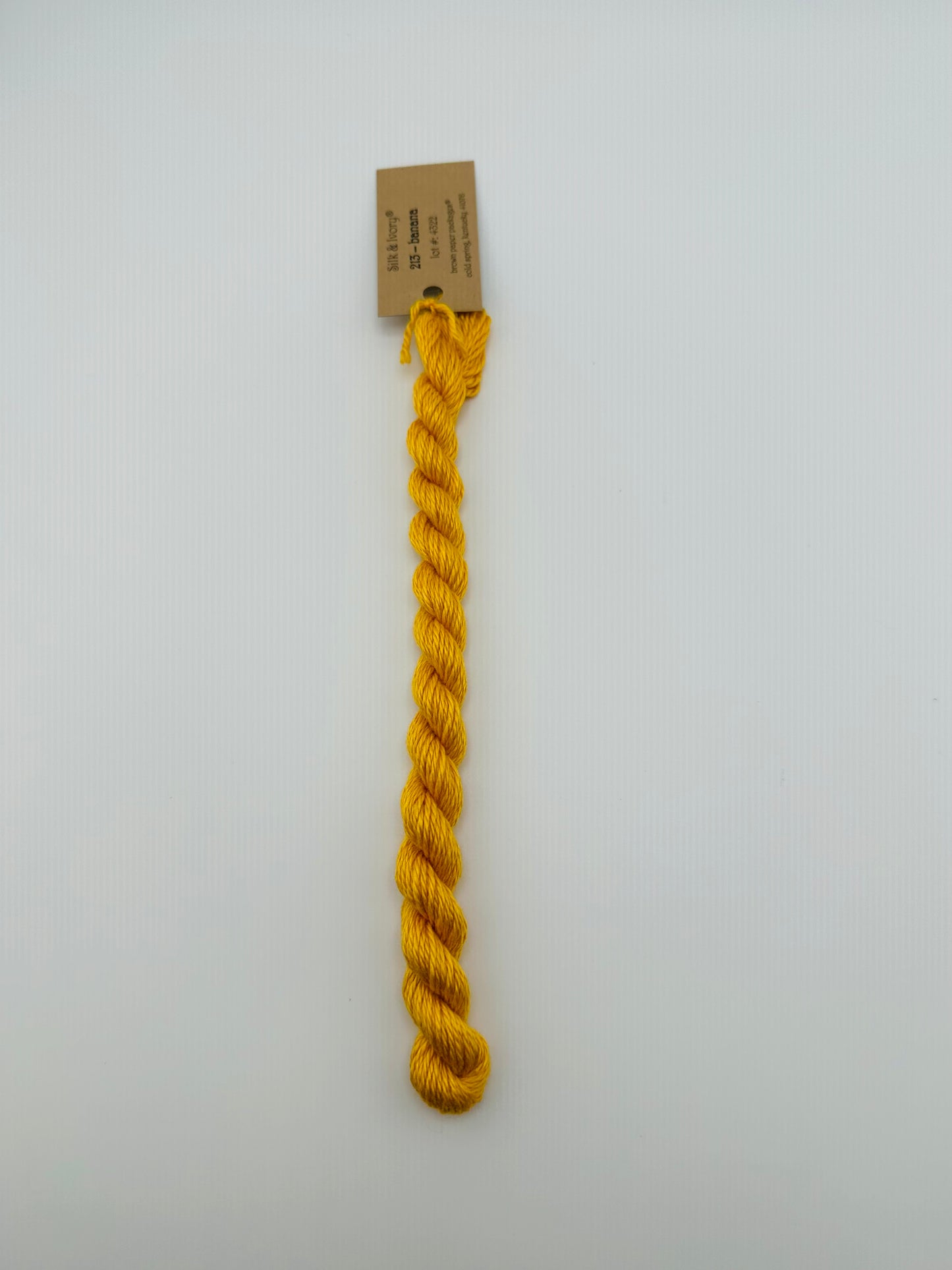 30 yard skein of silk & Ivory in the color 213 Banana with brown tag laying flat on white background