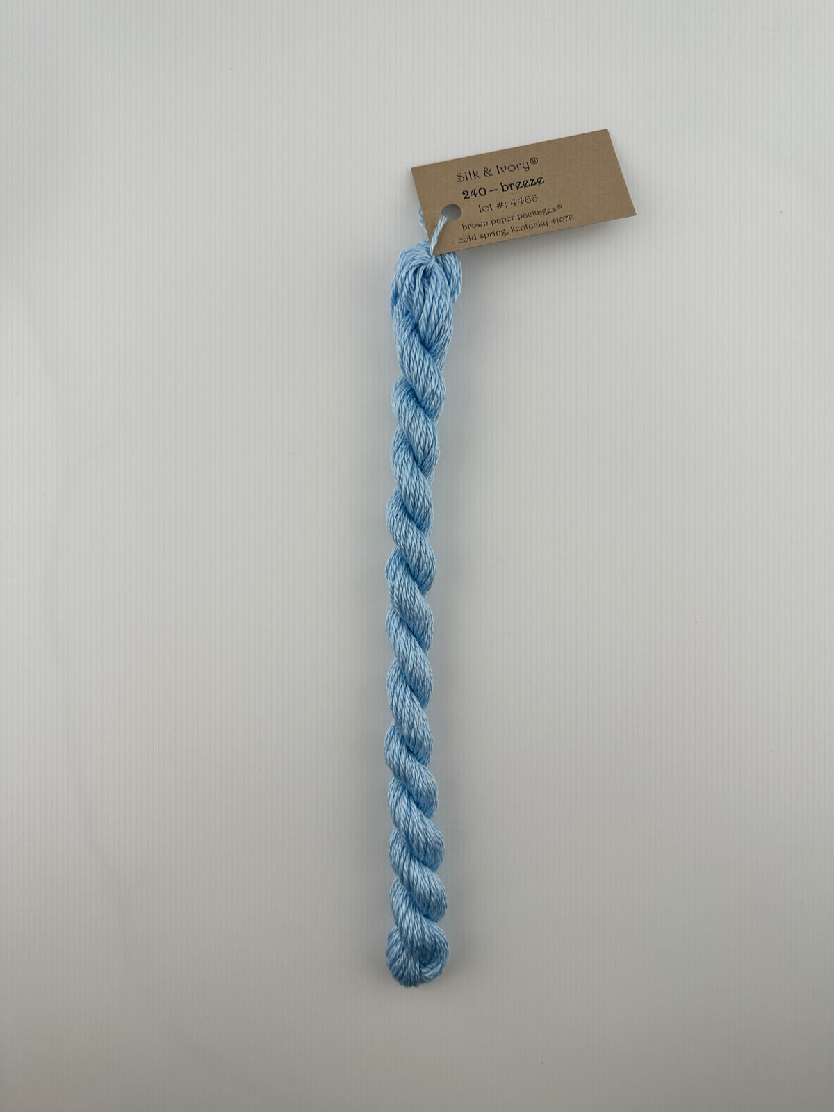 30 yard skein of silk & Ivory in the color 240 Breeze with brown tag laying flat on white background