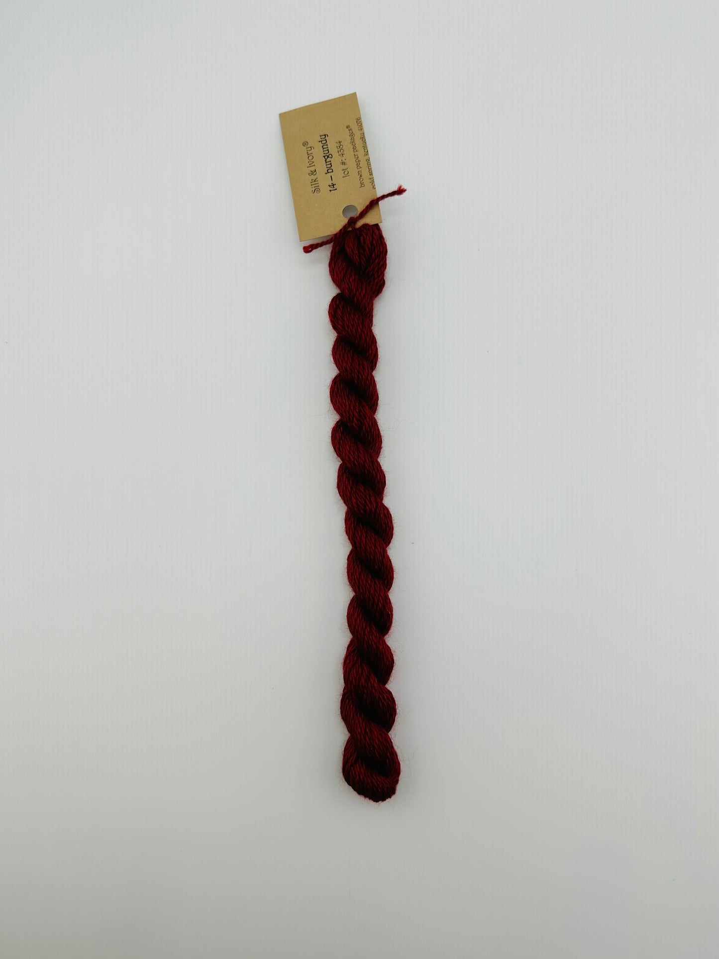 30 yard skein of silk & Ivory in the color 14 Burgundy with brown tag laying flat on white background