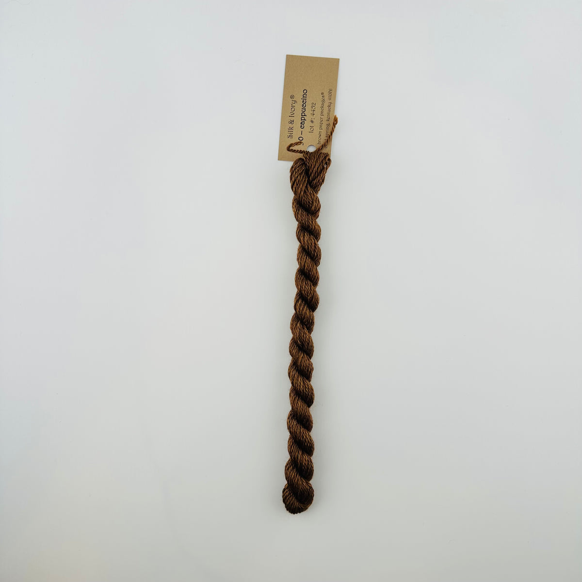 30 yard skein of silk & Ivory in the color 90 Cappuccino with brown tag laying flat on white background