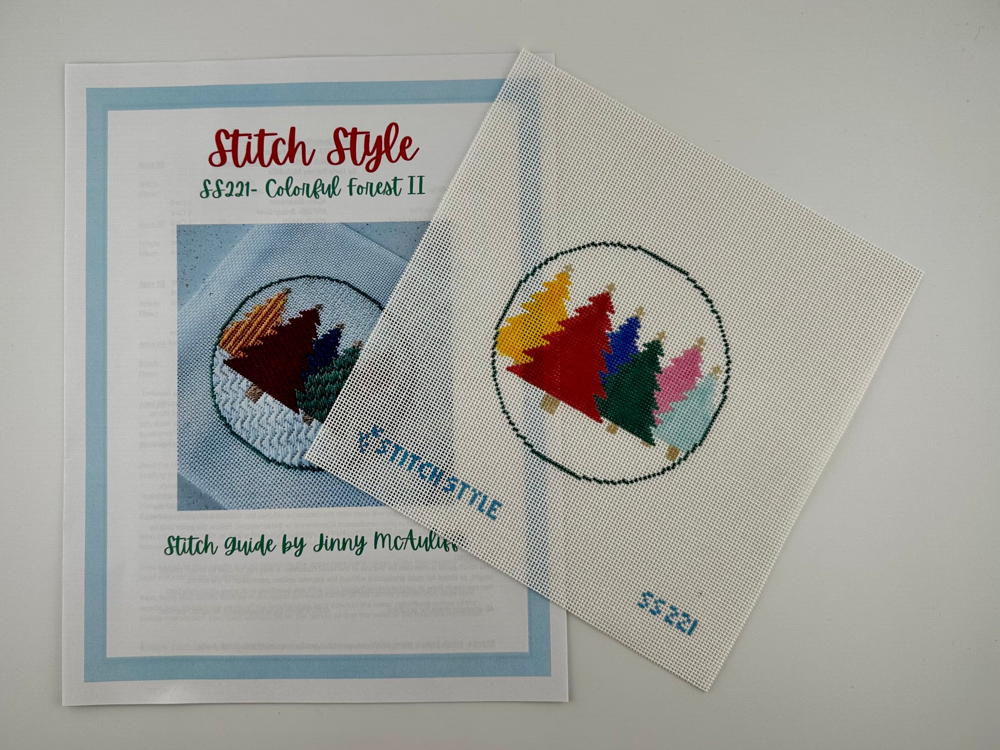 18 mesh needlepoint canvas featuring a circular design of six colorful Christmas trees in yellow, red, blue, green, pink, and light blue. The canvas has the brand name 'Stitch Style' and the number '55221' printed in blue at the bottom. Shown with stitch guide.