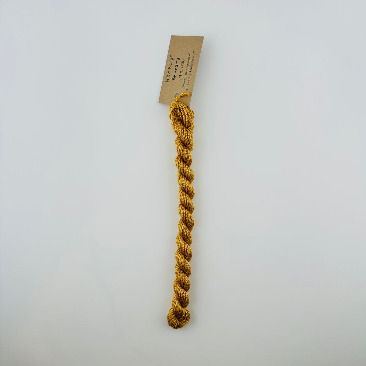 30 yard skein of silk & Ivory in the color 64 Curry with brown tag laying flat on white background
