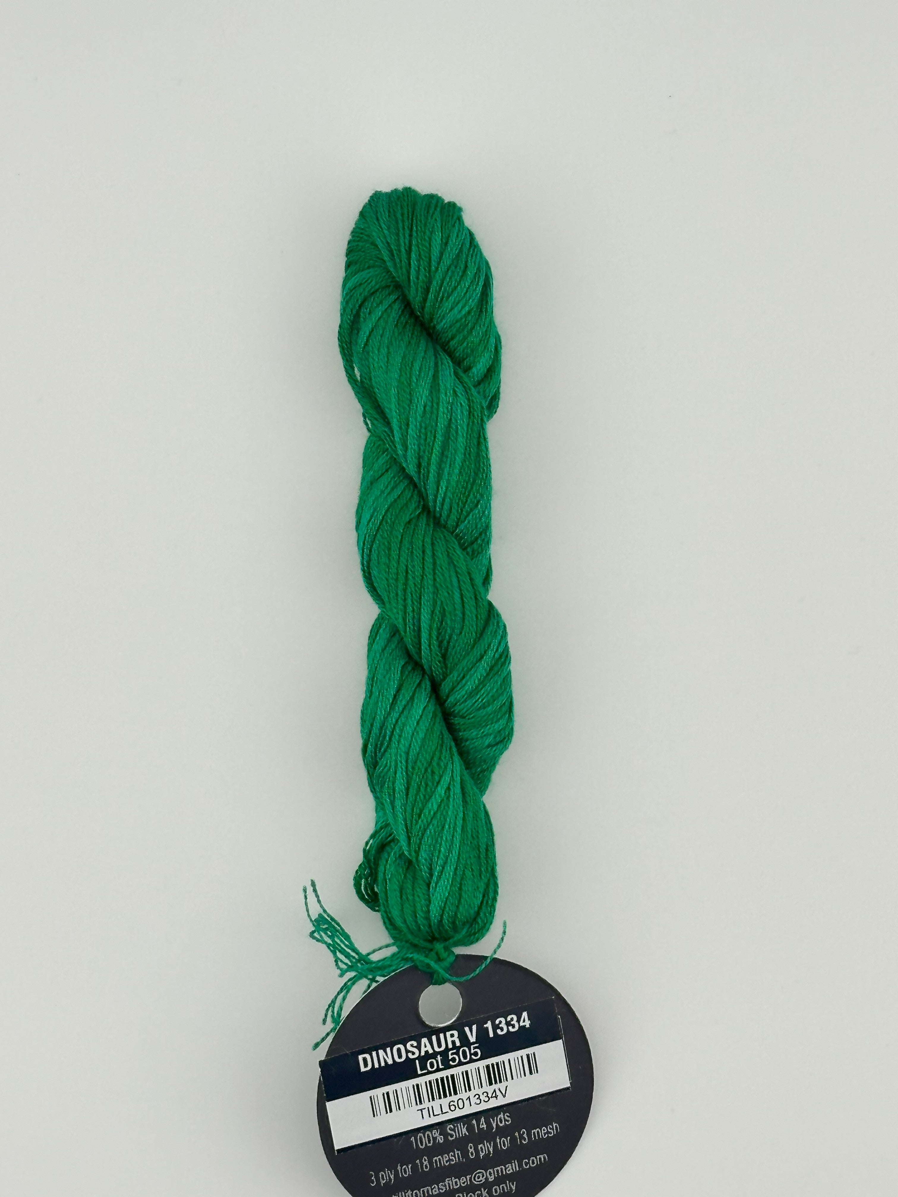 14 yard skein Planet Earth Silk 4 Ply needlepoint thread, in dinosaur v 1334  green with round black and white label lying flat on white background.