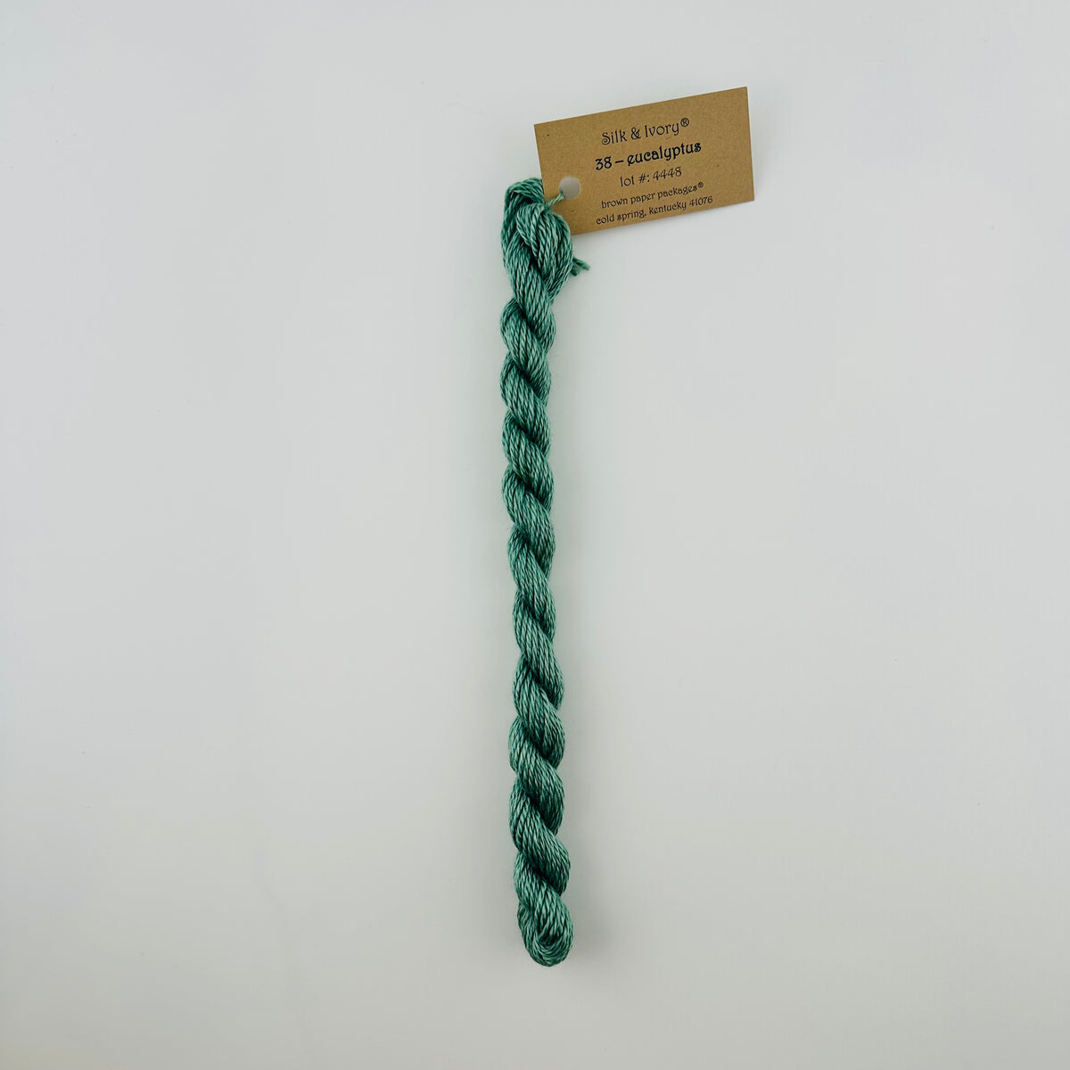 30 yard skein of silk & Ivory in the color 38 Eucalyptus with brown tag laying flat on white background