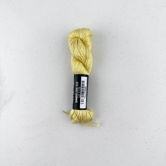 30 yard skein of Pepper Pot Silk needlepoint thread in a yellow variegated dandelion v229, with black and white label lying flat on white background
