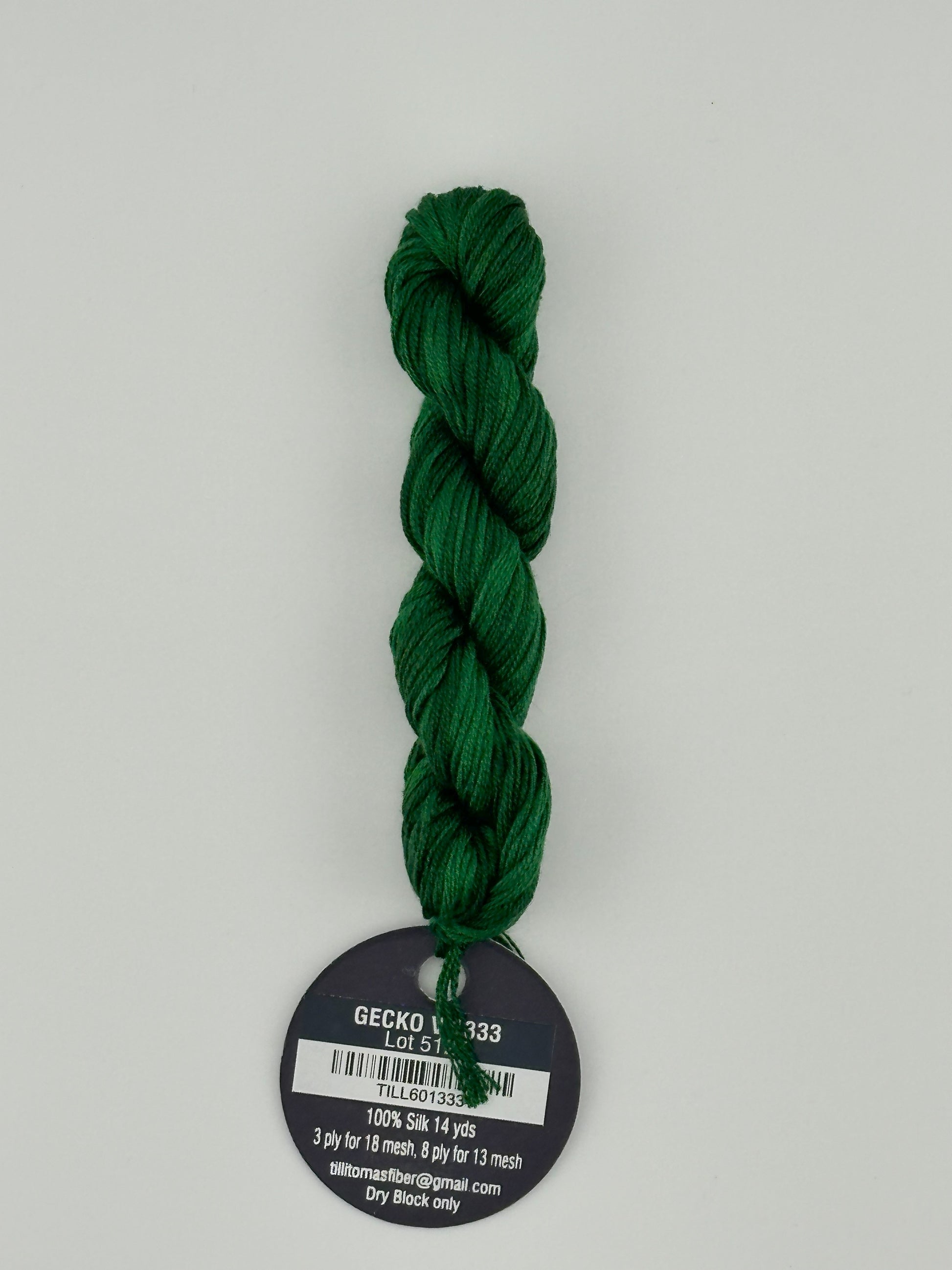 14 yard skein Planet Earth Silk 4 Ply needlepoint thread, in Gecko V 1333 green with round black and white label lying flat on white background.
