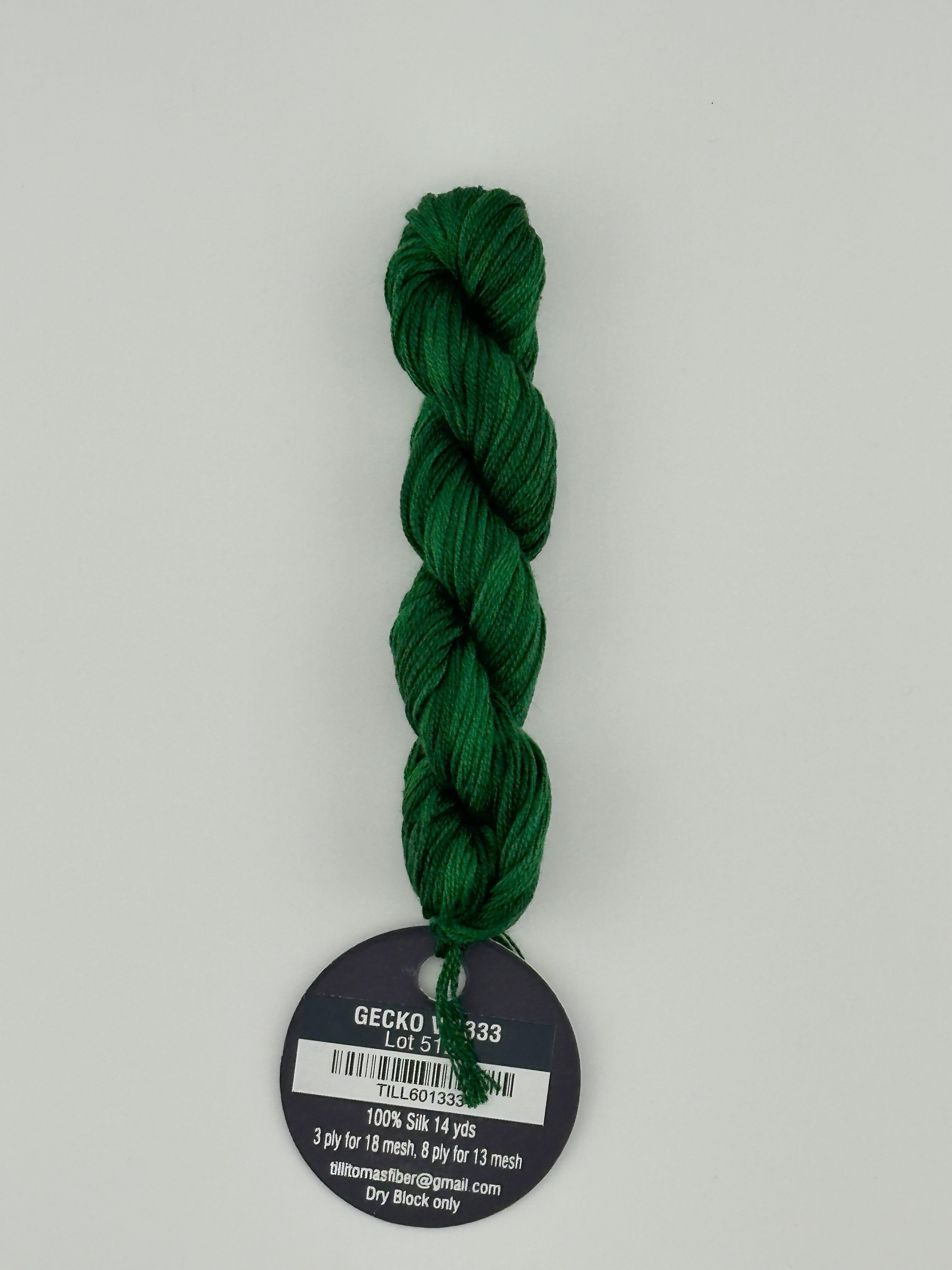 14 yard skein Planet Earth Silk 4 Ply needlepoint thread, in Gecko V 1333 green with round black and white label lying flat on white background.