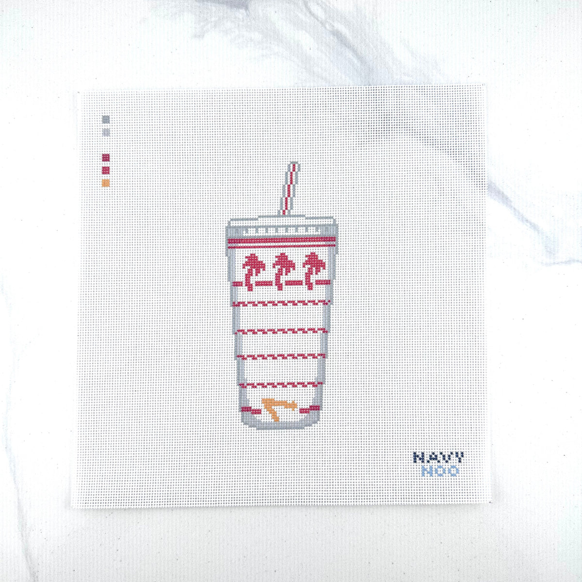 18 mesh needlepoint canvas design featuring a white paper cup with a red-and-white striped straw, palm tree motifs and red wavy line patterns . The canvas is photographed on a white marble-like surface, with the brand name 'NAVY NOO' printed in blue in the bottom right corner.