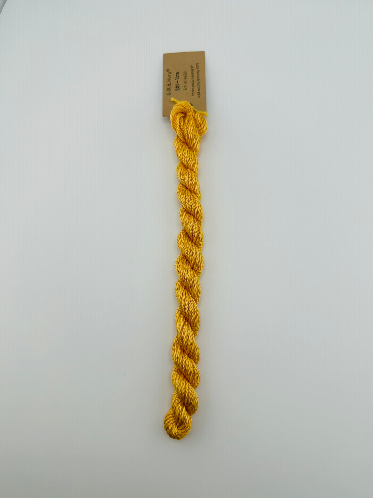 30 yard skein of silk & Ivory in the color 201 Lion with brown tag laying flat on white background