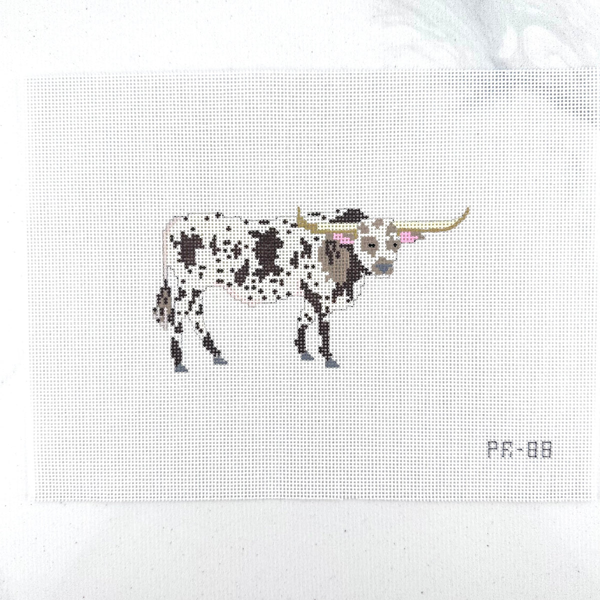 A needlepoint canvas featuring a brown and white spotted longhorn bull, displayed flat on a white backgroun