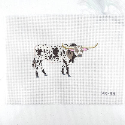 A needlepoint canvas featuring a brown and white spotted longhorn bull, displayed flat on a white backgroun