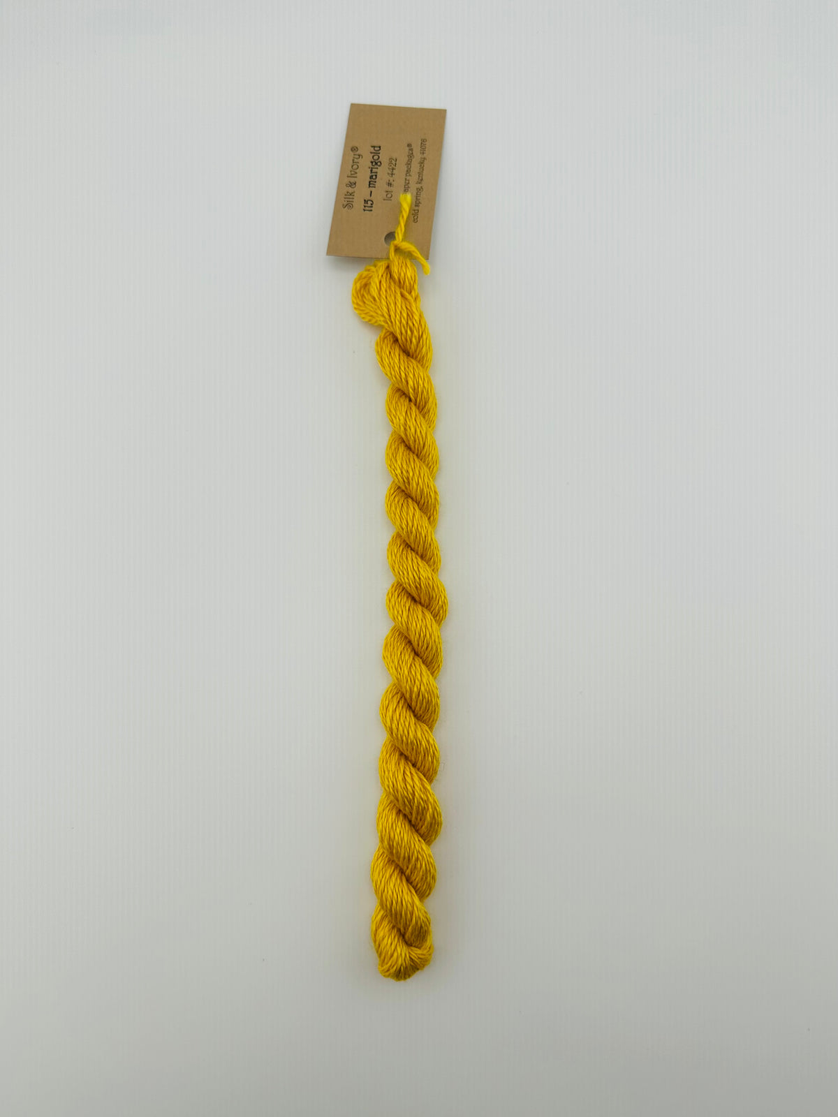 30 yard skein of silk & Ivory in the color 115 Marigold with brown tag laying flat on white background