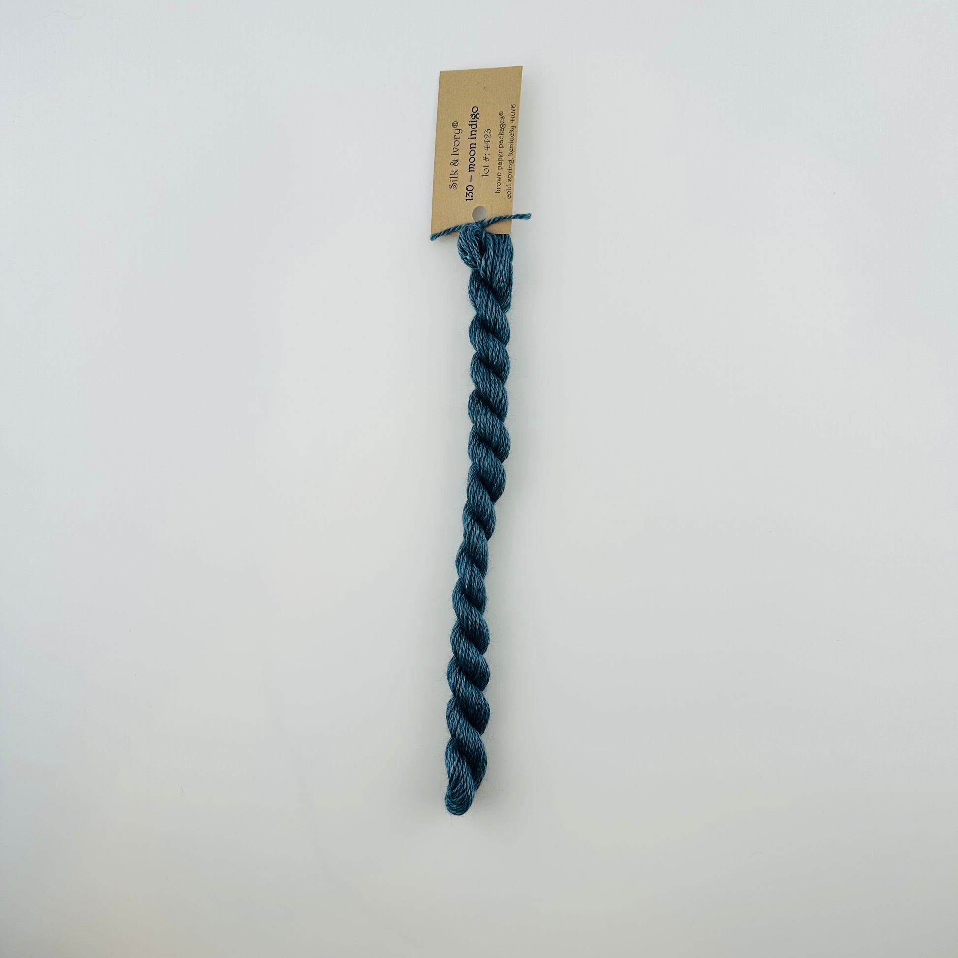 30 yard skein of silk & Ivory in the color 130 Moon Indigo with brown tag laying flat on white background
