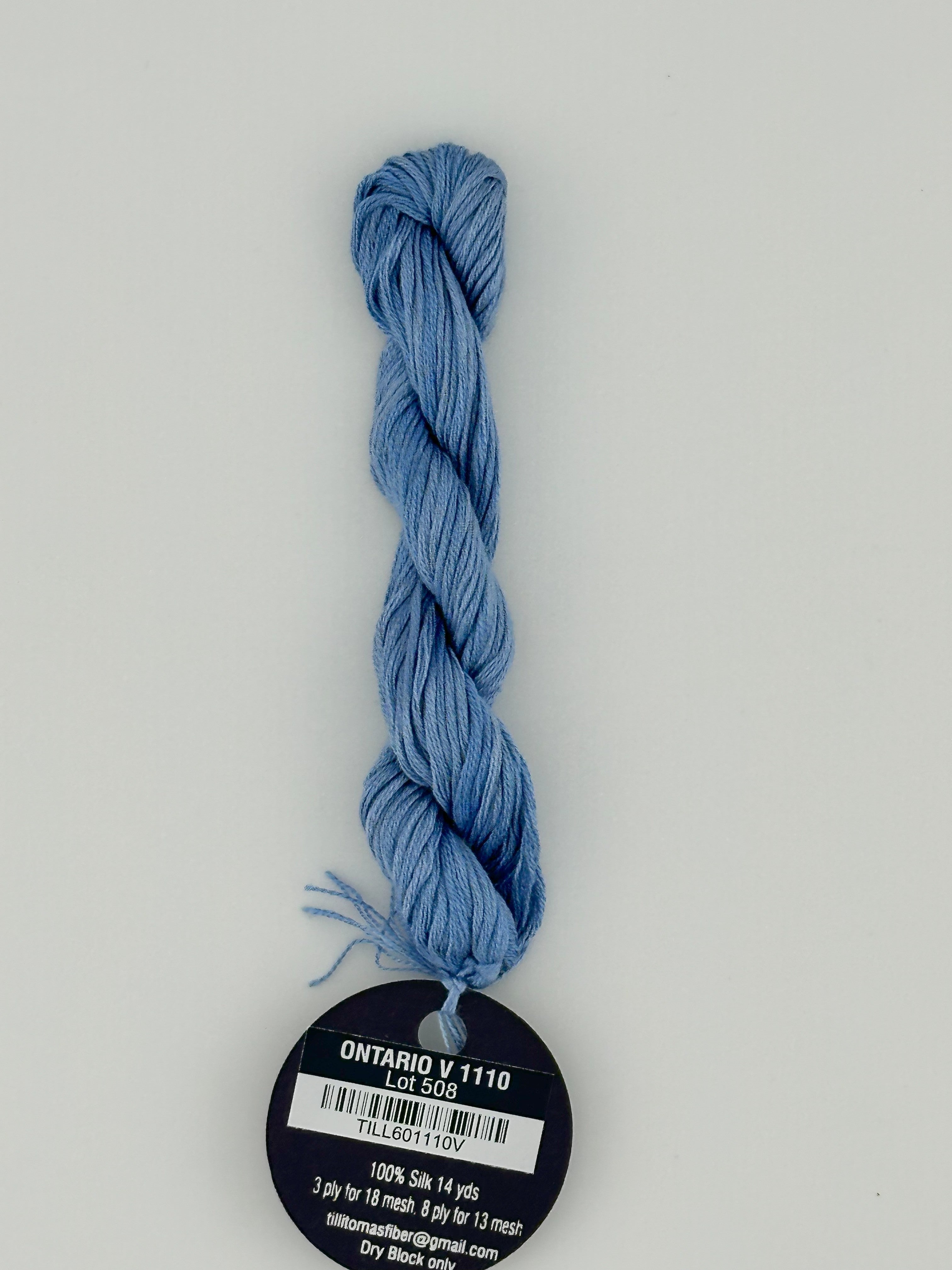 14 yard skein Planet Earth Silk 4 Ply needlepoint thread, in ontario v 1110, with round black and white label lying flat on white background.