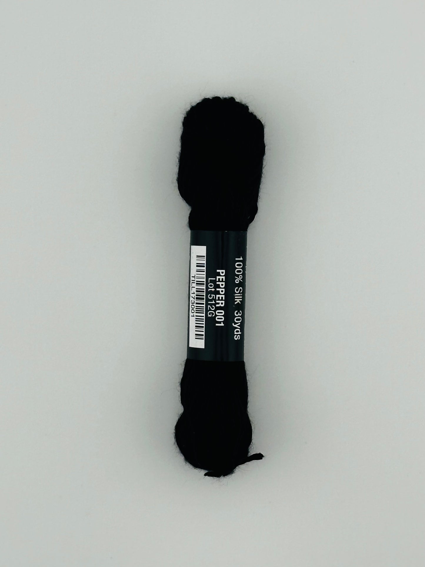 30 yard skein of Pepper Pot Silk needlepoint thread in pepper 001, with black and white label lying flat on white background