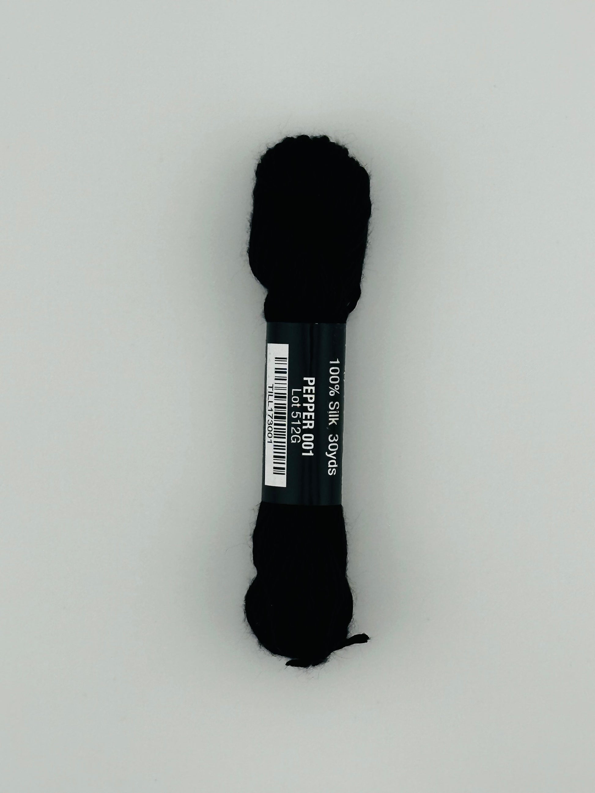 30 yard skein of Pepper Pot Silk needlepoint thread in pepper 001, with black and white label lying flat on white background