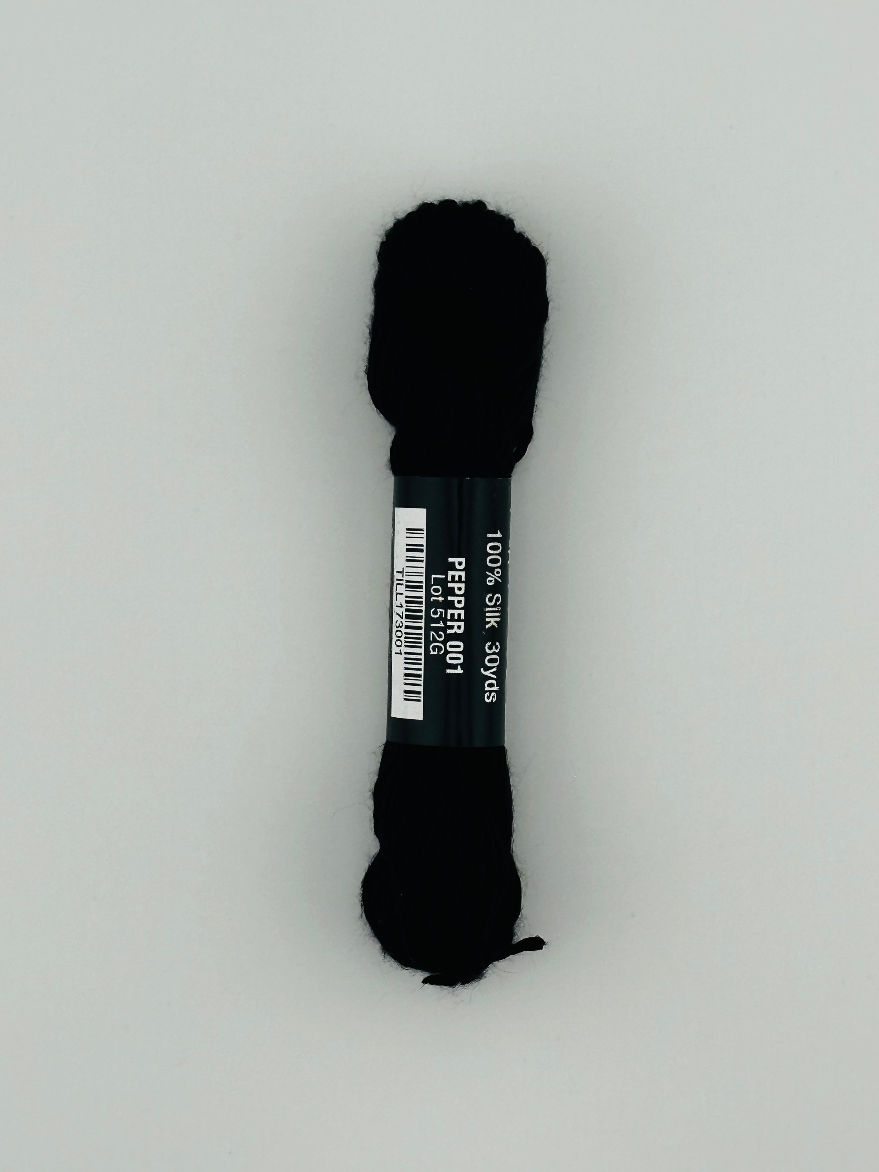 30 yard skein of Pepper Pot Silk needlepoint thread in pepper 001, with black and white label lying flat on white background